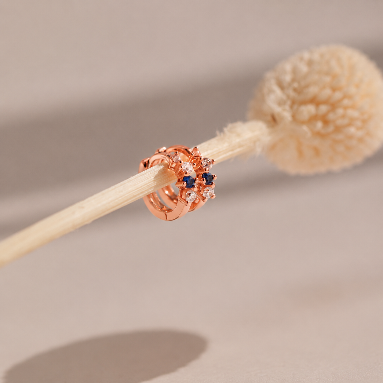 Rose gold ring with blue gemstone on a wooden stick against a neutral background